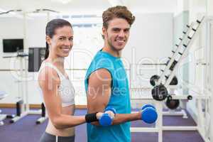 Fit couple exercising with blue dumbbells smiling at camera