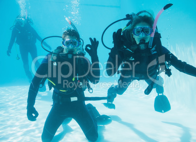 Friends on scuba training submerged in swimming pool two looking