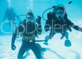 Friends on scuba training submerged in swimming pool two looking