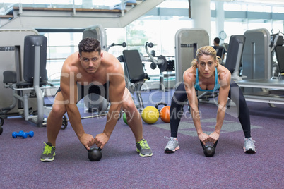 Bodybuilding man and woman lifting kettlebells in a squat