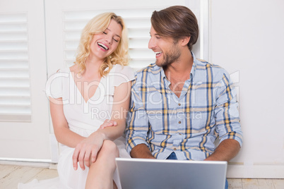 Happy couple sitting on floor using laptop