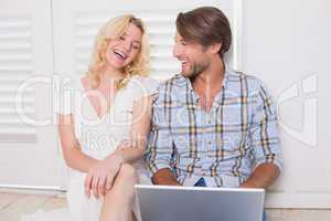 Happy couple sitting on floor using laptop