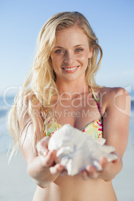 Pretty blonde in bikini holding conch on the beach