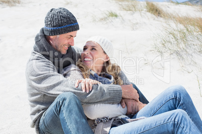 Attractive couple smiling at each other on the beach in warm clo