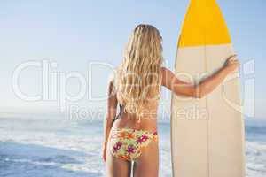 Gorgeous blonde surfer in bikini holding her board