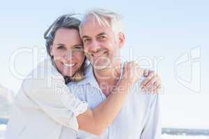 Attractive couple hugging at the beach smiling at camera