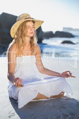 Beautiful blonde in sundress sitting in lotus pose on the beach