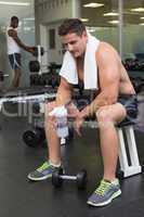 Shirtless bodybuilder holding protein drink sitting on bench