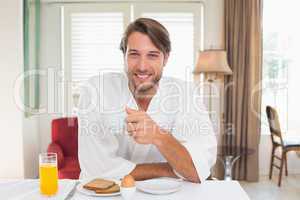 Handsome man having breakfast in his bathrobe smiling at camera