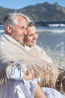 Smiling couple sitting on the beach under blanket