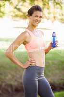 Fit woman holding water bottle in the park smiling at camera