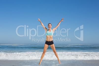 Fit woman jumping on the beach with arms out Fit woman jumping on the beach with arms out