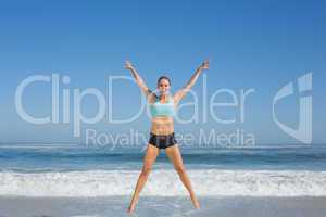 Fit woman jumping on the beach with arms out