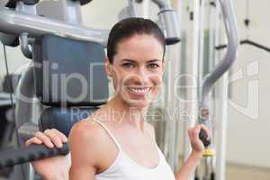 Fit brunette using weights machine for arms smiling at camera