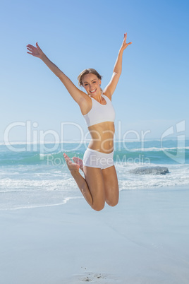 Gorgeous fit blonde jumping by the sea with arms out