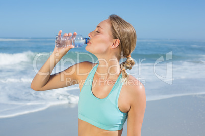 Fit woman standing on the beach taking a drink