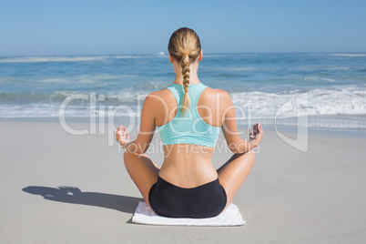 Fit woman sitting on the beach in lotus pose