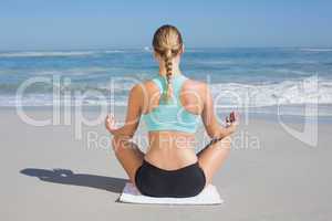 Fit woman sitting on the beach in lotus pose