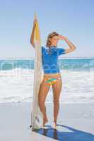 Fit smiling surfer girl standing on the beach with her surfboard