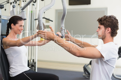 Fit brunette using weights machine for arms with trainer helping