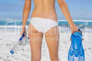 Rear view of fit woman holding fins and snorkel on the beach