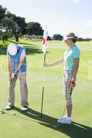 Lady golfer holding eighteenth hole flag for partner putting bal