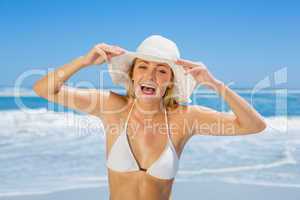 Smiling blonde in white bikini and sunhat on the beach