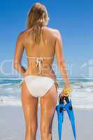 Fit woman in white bikini holding snorkeling gear on the beach