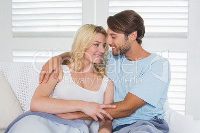 Cute casual couple sitting on couch under blanket