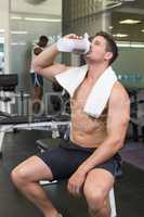Shirtless bodybuilder drinking protein drink sitting on bench