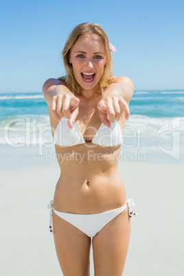 Beautiful blonde smiling and pointing at camera on the beach