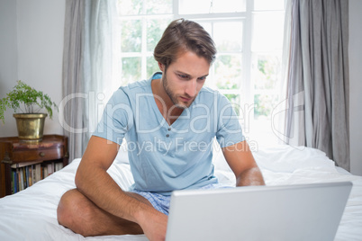 Handsome man sitting on bed using laptop