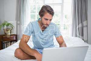 Handsome man sitting on bed using laptop