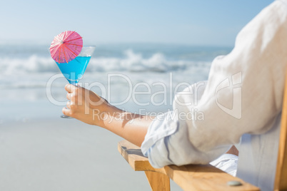 Woman relaxing in deck chair by the sea holding cocktail