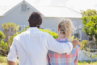 Cute couple standing together in their garden looking at house