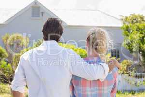 Cute couple standing together in their garden looking at house