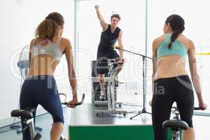 Fit women doing a spin class with enthusiatic instructor