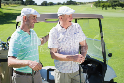 Golfing friends standing beside their buggy smiling