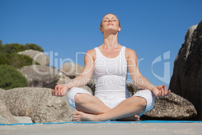 Blonde woman sitting in lotus pose on beach on mat