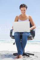 Pretty brunette using laptop on the beach sitting on swivel chai