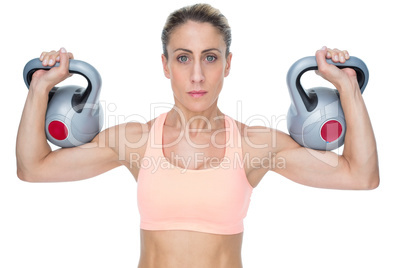 Serious female crossfitter lifting kettlebells looking at camera