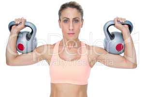 Serious female crossfitter lifting kettlebells looking at camera