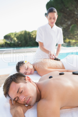 Attractive couple enjoying hot stone massage poolside