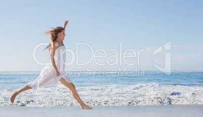 Beautiful blonde in white sundress jumping up on the beach