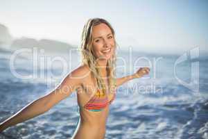 Content blonde standing on the beach in bikini with arms out