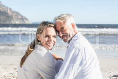 Couple sitting on the beach under blanket smiling at camera