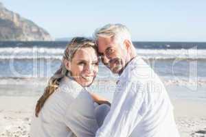 Couple sitting on the beach under blanket smiling at camera