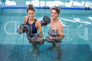 Man and woman standing with foam dumbbells in the pool