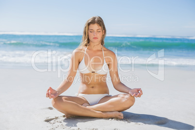 Beautiful girl in white bikini sitting in lotus pose on beach