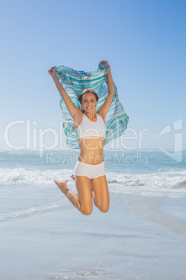 Gorgeous fit blonde jumping by the sea with scarf